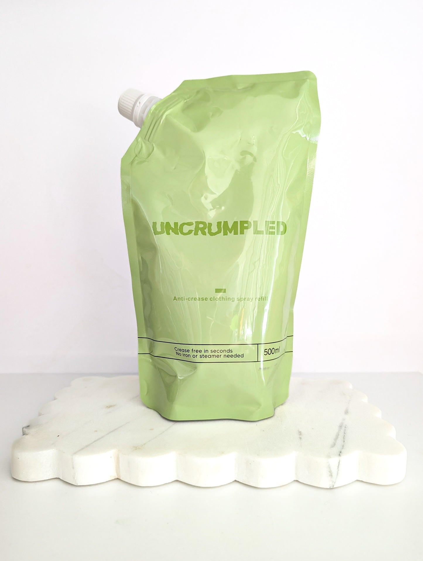 Green Uncrumpled refill pouch standing on a white platform against a white background.