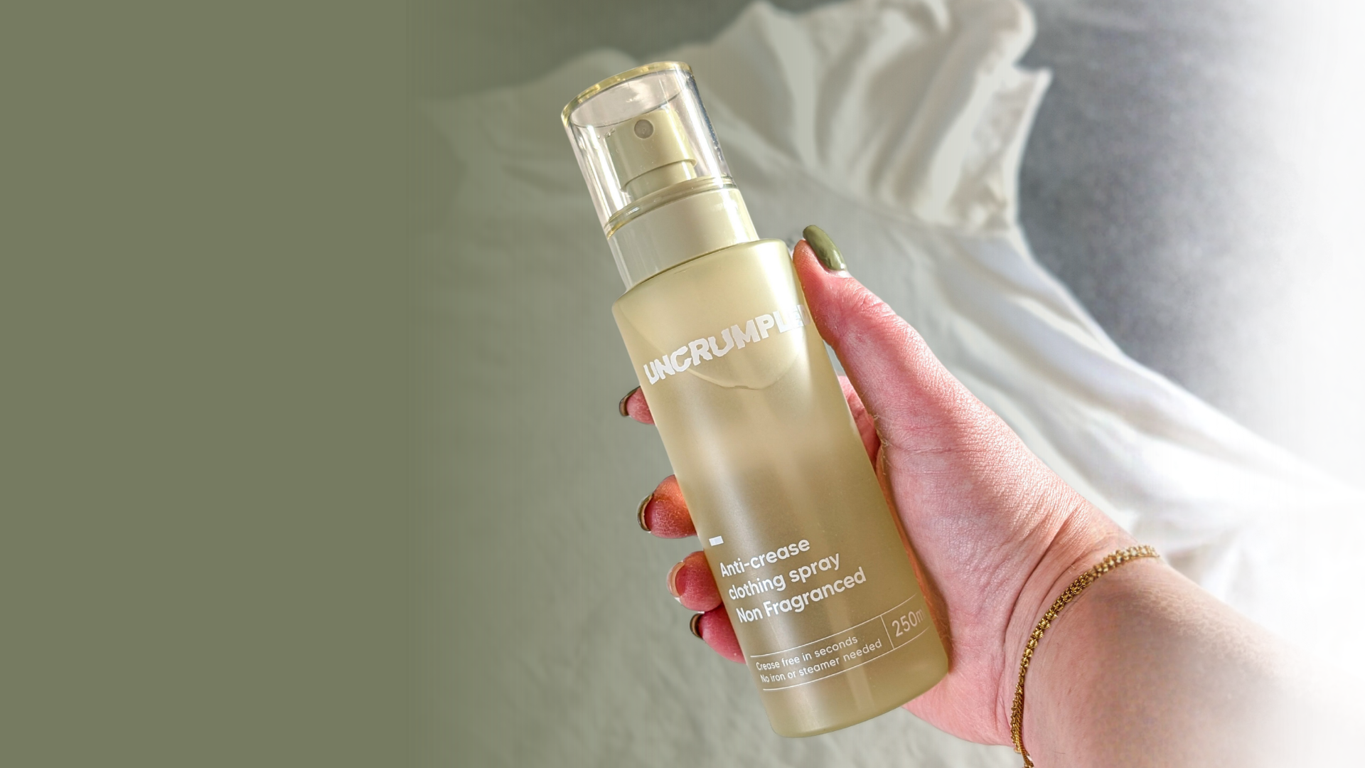 Hand holding a regular-sized 250ml Uncrumpled anti-crease spray bottle against a background featuring a white shirt draped on a flat surface.